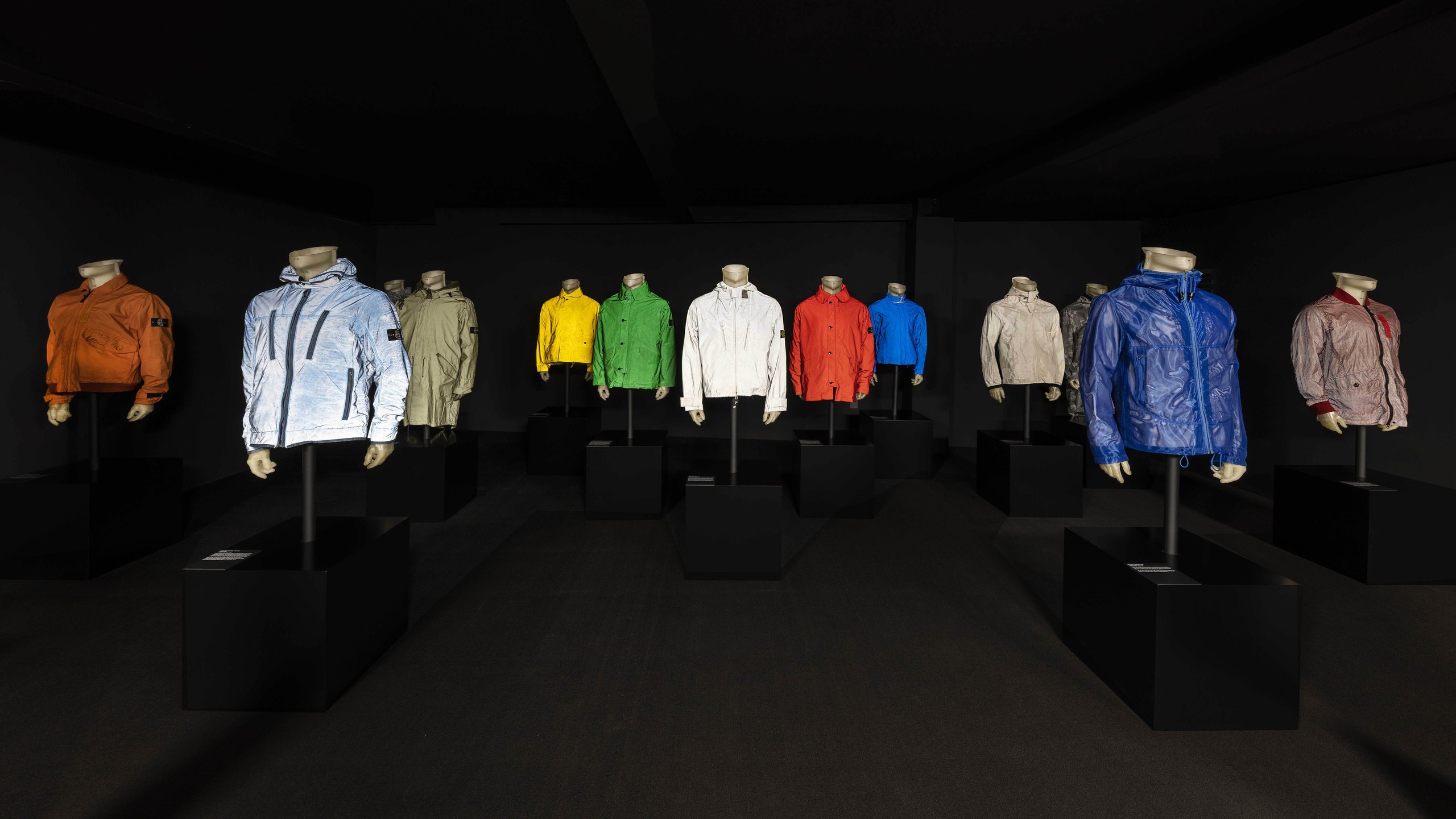 A room of Stone Island reflective and metallic jackets lit against black
